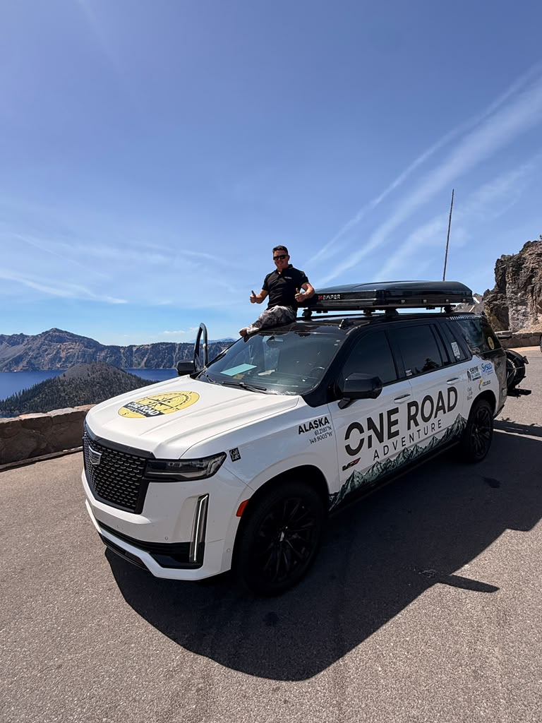 The One Road Adventure vehicle marked with Alaska coordinates, overlooking a mountain lake.
